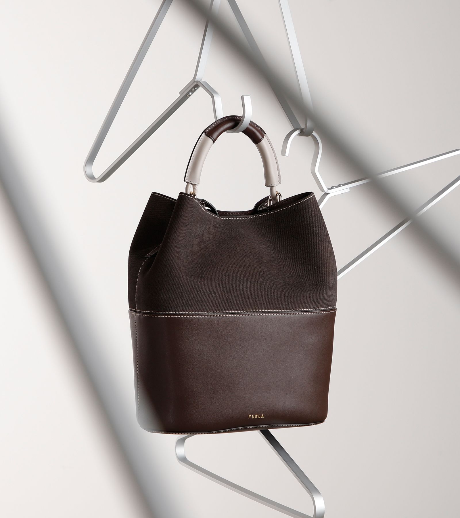 Dunkelbraune Eimertasche mit Metallgriff, zwischen Kleiderbügeln aufgehängt