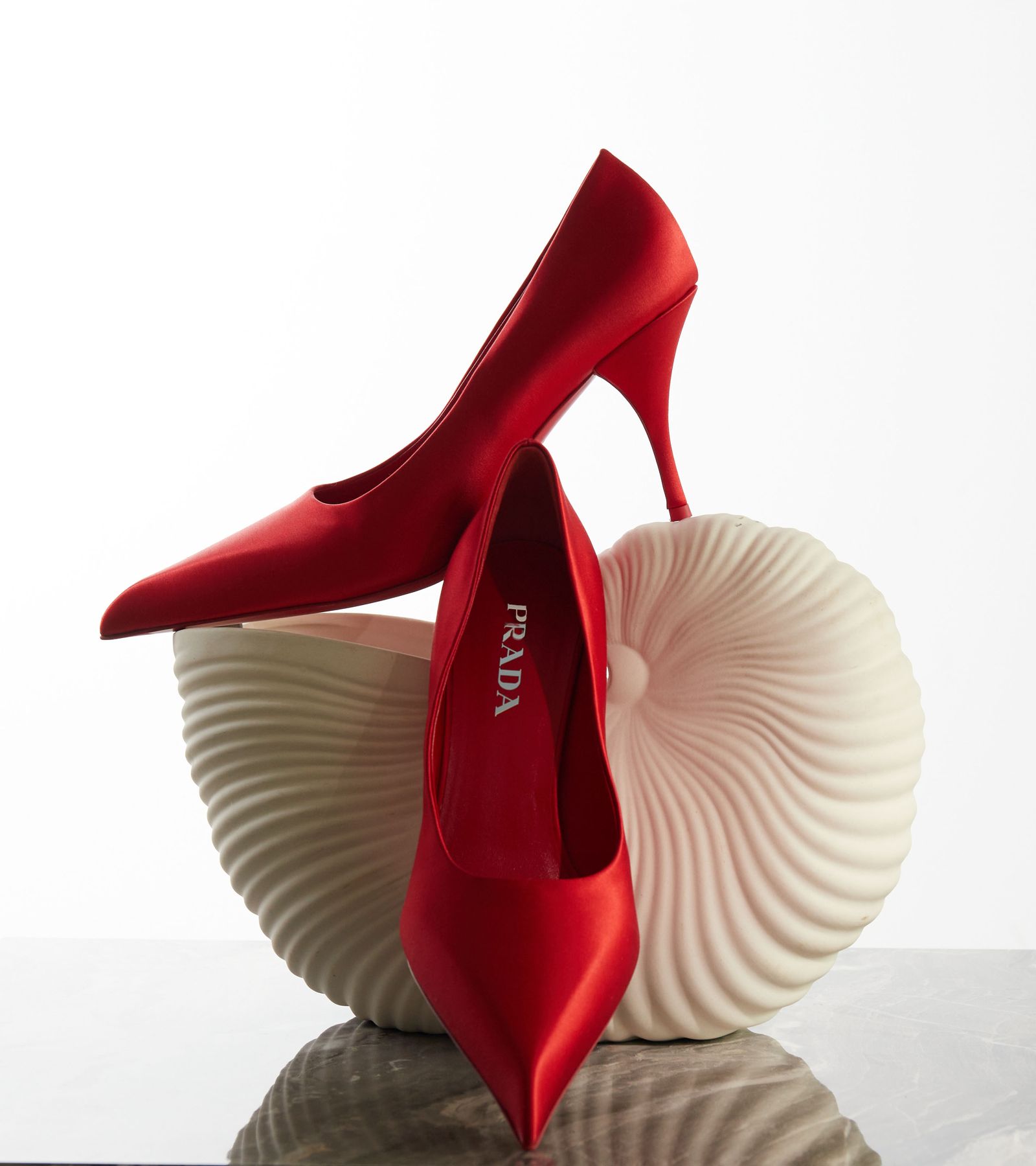 Rote Satin-Pumps von Prada auf einer Muschelskulptur