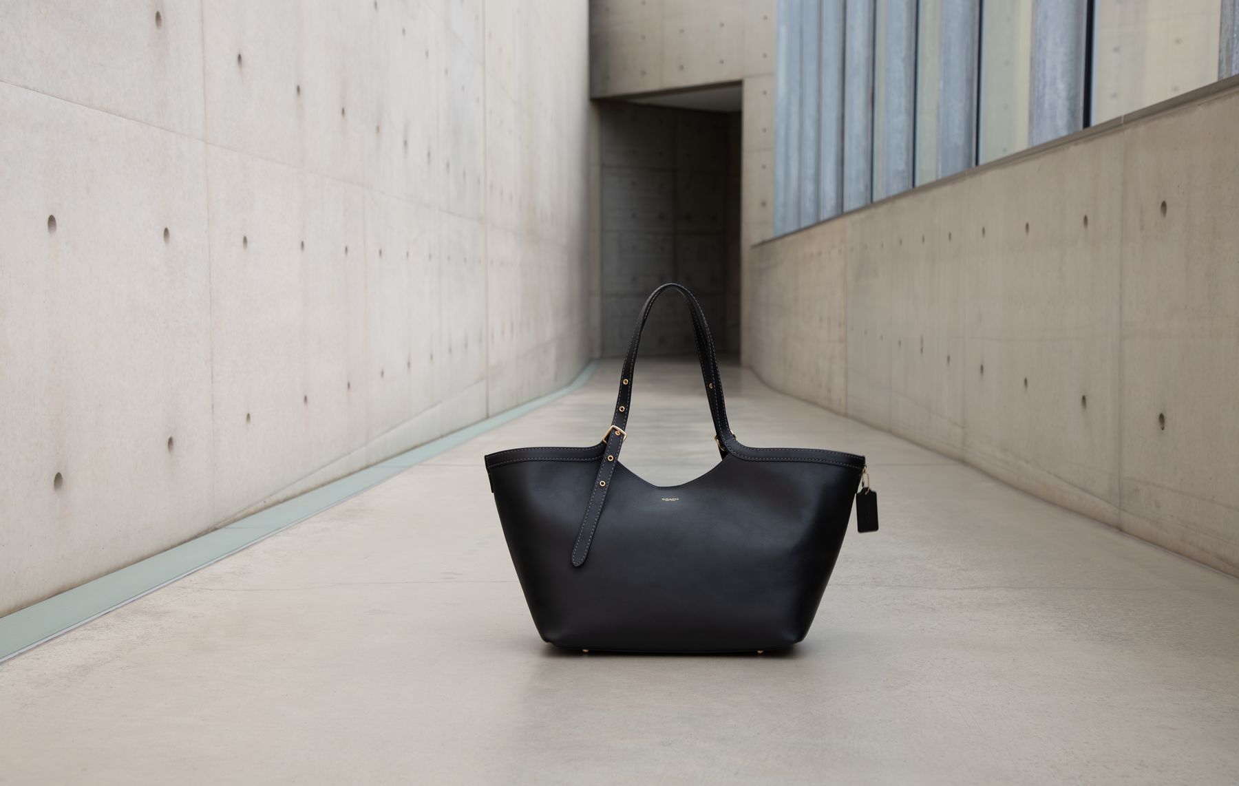 Schwarze Tasche in einem Betongang mit Fensterband im Hintergrund