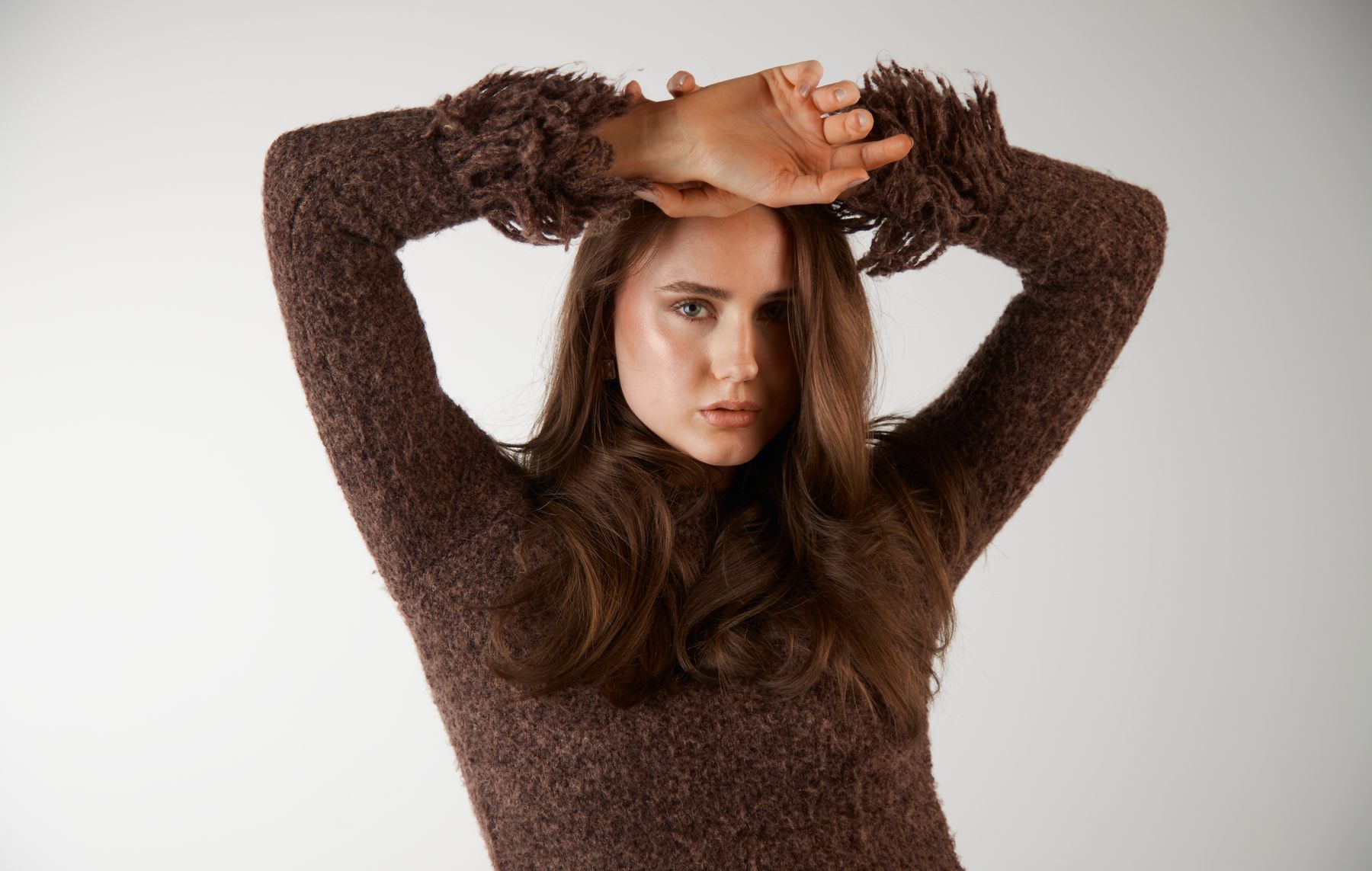 Model in braunem Strickpullover, Arme über dem Kopf